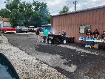 BBQ grill with several people cooking and setting things up.